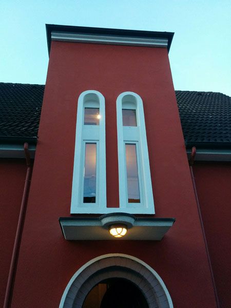 zwei schmale lange weiße Rundbogenfenster der einer Eingangstür auf dunkelroter Fassade